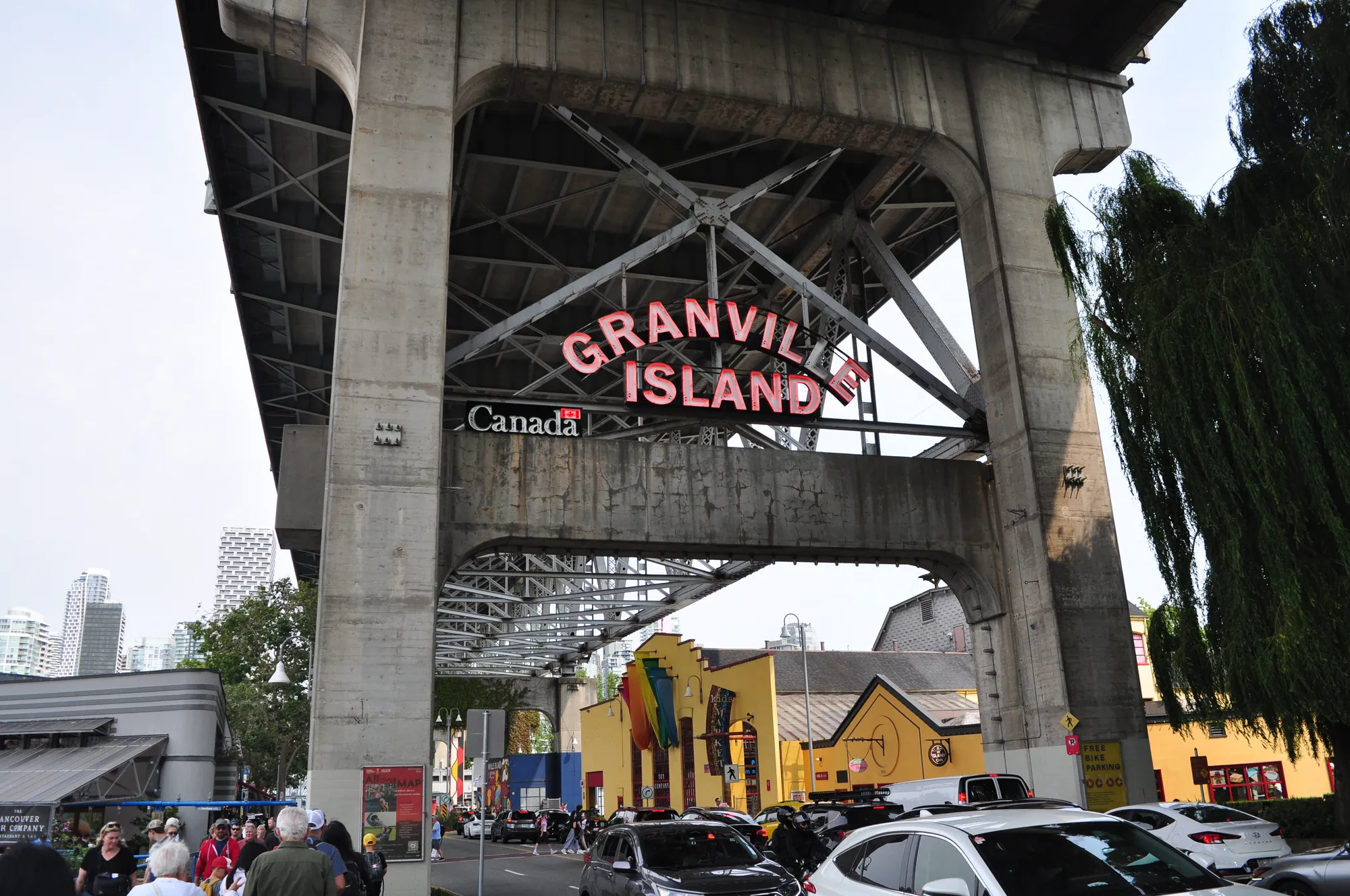 Granville Island neon sign under the bridge with skyline in Vancouver