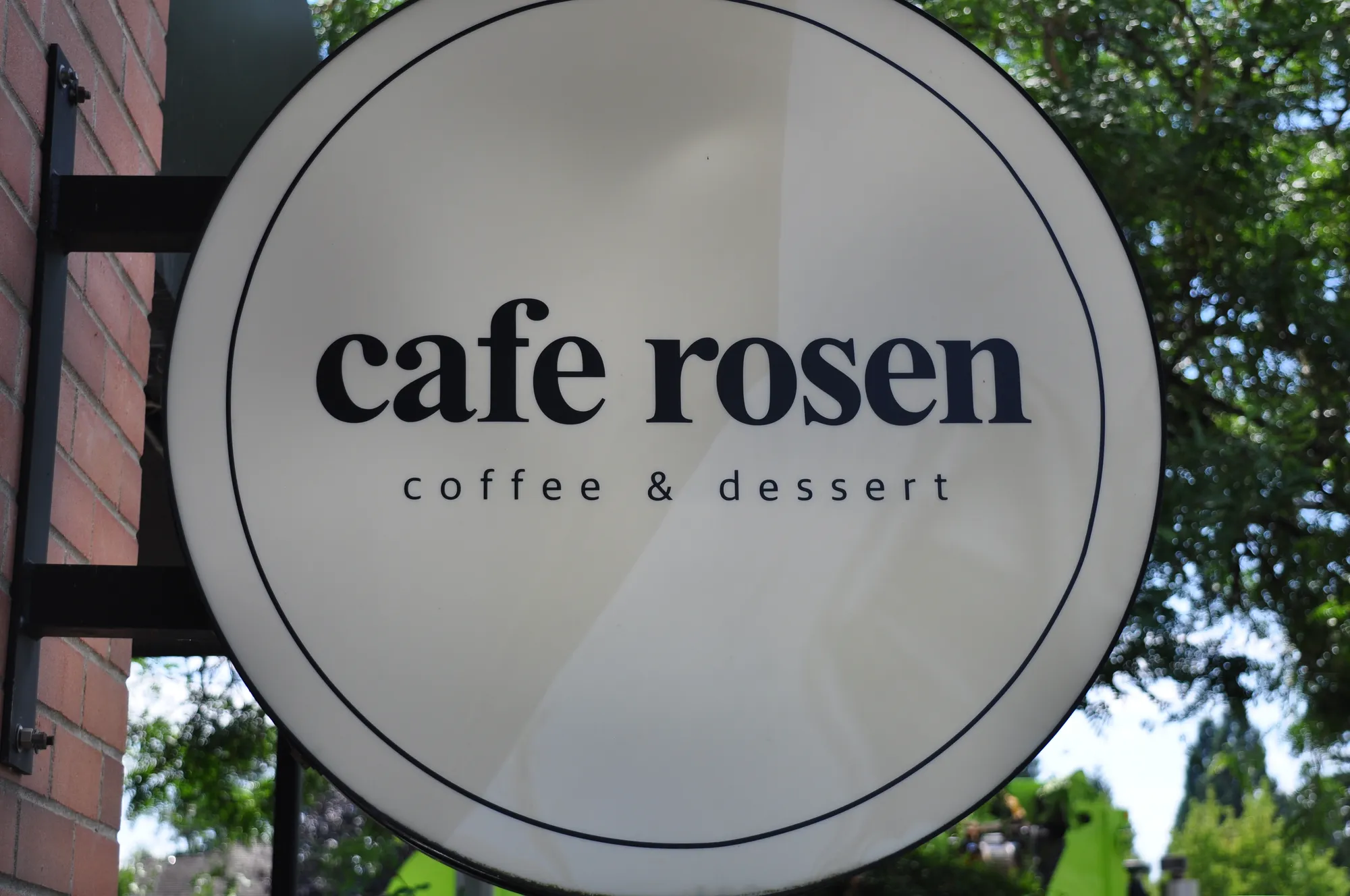 Round illuminated cafe rosen blade sign on brick storefront in Vancouver